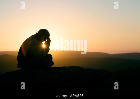 Profilo di Silhouette di un orante seduto su una collina di sunrise Foto Stock