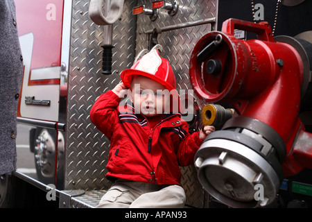 Bambino in vigili del fuoco hat seduta su camion dei pompieri Foto Stock