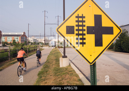 Due ciclisti su un rail trail lontano di equitazione con un cartello di avvertimento o di ferrovia via del pericolo in primo piano nel Conshohocken Pennsylvania Foto Stock