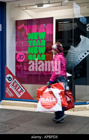 Donna con capelli tinti che trasportano la vendita di plastica Sacchi passato a piedi una scarpa store pubblicità loro 2008 gennaio vendite a Dundee, Regno Unito Foto Stock