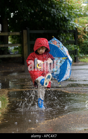 Little Boy in cappotto rosso e blu di spruzzi di ombrello in caso di pioggia Foto Stock