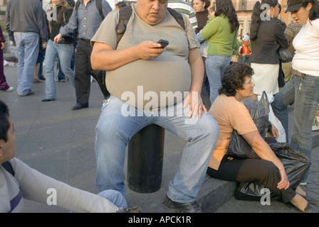 Un sovrappeso obesi uomo compone il suo telefono celular mentre seduto su un posto vicino al Zocaló o plaza principale nel centro di Città del Messico Foto Stock