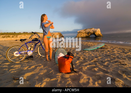 Una donna di medicazione sulla spiaggia al tramonto dopo la navigazione a Natural Bridges State Park a Santa Cruz California Foto Stock