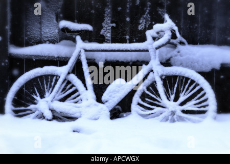 Una bicicletta con neve accanto a una recinzione. Foto Stock