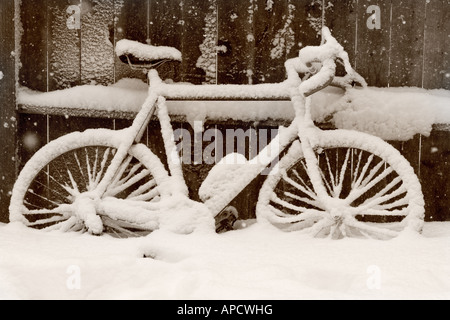 Una bicicletta con neve accanto a una recinzione. Foto Stock