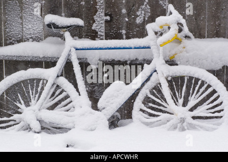 Una bicicletta con neve accanto a una recinzione. Foto Stock