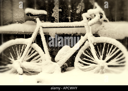 Una bicicletta con neve accanto a una recinzione. Foto Stock