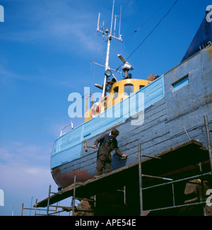 L'uomo ribadendo una barca da pesca in un cantiere di riparazione navale, Grimsby, Humberside, Inghilterra, Regno Unito. Foto Stock