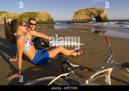 Un giovane, una tavola da surf e una bicicletta presso la spiaggia di ponti naturali del Parco Statale di Santa Cruz, California Foto Stock