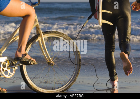 Una donna su un cruiser bike e un uomo con una tavola da surf sulla spiaggia di ponti naturali del Parco Statale di Santa Cruz in California Foto Stock