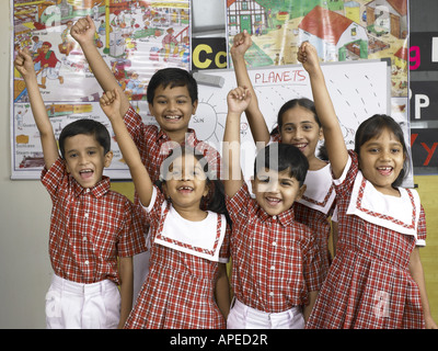 South Asian Indian i ragazzi e le ragazze in piedi insieme con il sollevamento di mani nella scuola materna MR Foto Stock