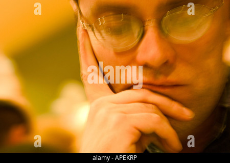 Primo piano di un giovane uomo, indossando occhiali, con la sua testa in appoggio sulla sua mano. Foto Stock