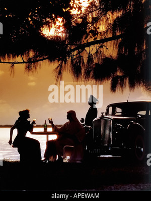 Giovane silhouette (uomo vestito come Arabian sheik, donna in elegante abito occidentale) la tostatura con bottiglia e bicchieri di vino Foto Stock