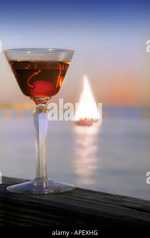 Il Vermouth bere e vetro close-up, cherry interno, sulla trave di legno con fiery tramonto e barca a vela in oceano in background. Foto Stock