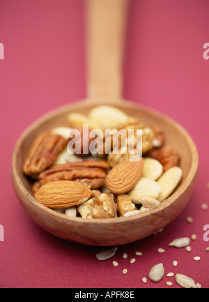 Selezione di noci e semi su un cucchiaio di legno scuro su sfondo viola Foto Stock