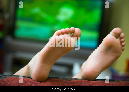 Bambino sdraiato sul divano con i piedi in aria Foto Stock