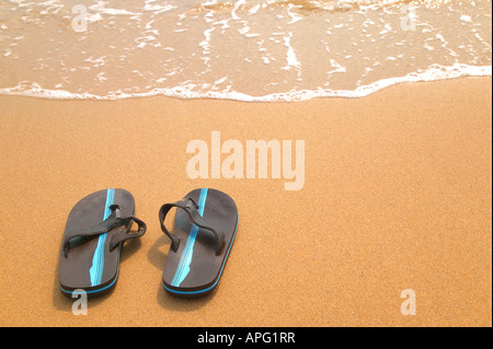 Una coppia di flip flop su una spiaggia di sabbia fine e dorata dal bordo delle acque Foto Stock