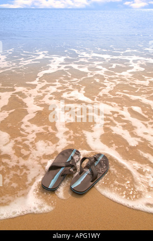 Una coppia di flip flop su una spiaggia di sabbia dorata di essere lavato fuori in mare una leggera sfocatura del movimento Foto Stock