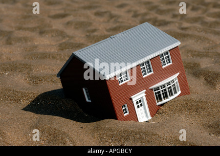 Modello giocattolo casa affondando nella sabbia Foto Stock