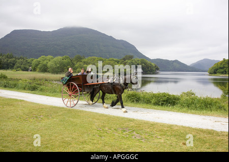 Due turisti femmina prendere un cavallo e trappola jaunting cavalcare carrello accanto ai laghi di Killarney di Muckross Abbey Foto Stock
