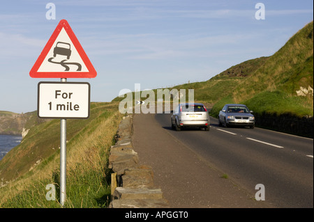Triangolare foderato rosso strada sdrucciolevole per un miglio avvertenza cartello stradale sulla A2 strada costiera con le automobili vicino Dunluce Castle Foto Stock
