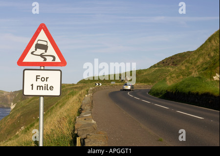 Triangolare foderato rosso strada sdrucciolevole per un miglio avvertenza cartello stradale sulla A2 strada costiera con auto a piegare vicino Dunluce Castle Foto Stock