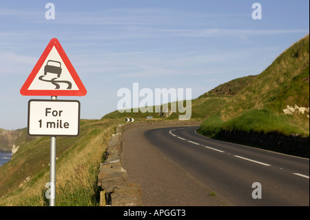 Triangolare foderato rosso strada sdrucciolevole per un miglio avvertenza cartello stradale sulla A2 coast road a piegare vicino Dunluce Castle Foto Stock
