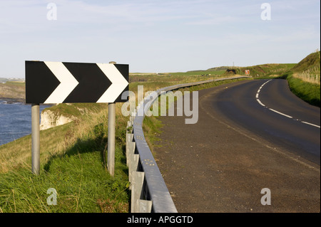 Bianco e nero chevron forte deviazione a destra cartello stradale nei pressi di curva pericolosa a strapiombo sulla A2 coast road vicino Dunluce Foto Stock