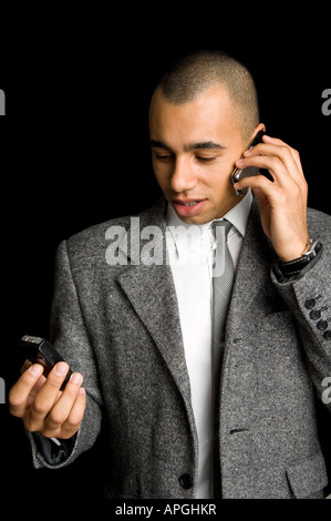 Giovani razza mista imprenditore chattare su due telefoni cellulari Foto Stock