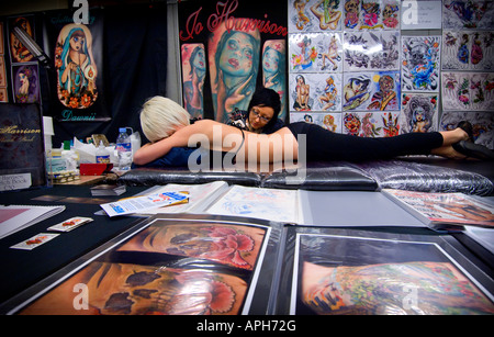 Alla prima relazione annuale di Brighton Tattoo Convention Tattoo Artist Jo Harrison lavora su un client circondato dalla sua tecnica flash Foto Stock