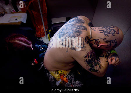 Un artista del tatuaggio al lavoro che affonda un disegno sulla schiena di un uomo. Foto di Jim Holden. Foto Stock