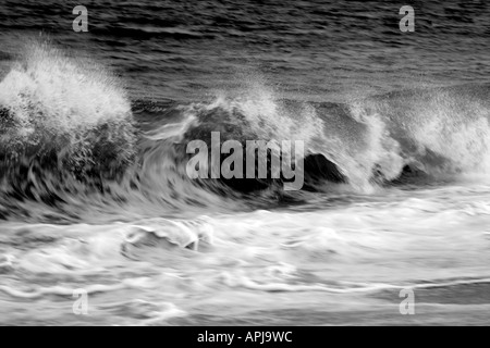 Un oceano onda di schiantarsi sulla riva con spruzzi provenienti dalla parte superiore della forma d'onda. Una fotografia in bianco e nero Foto Stock