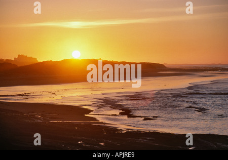 Spiaggia con il castello di BAMBURGH e Isola Santa VISTA DA SEAHOUSES AL TRAMONTO NORTHUMBERLAND REGNO UNITO Foto Stock
