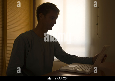 Uomo in silhouette seduti nella parte anteriore del computer portatile Foto Stock