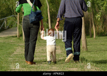 Baby girl ad imparare a camminare aiutato dai suoi genitori Foto Stock