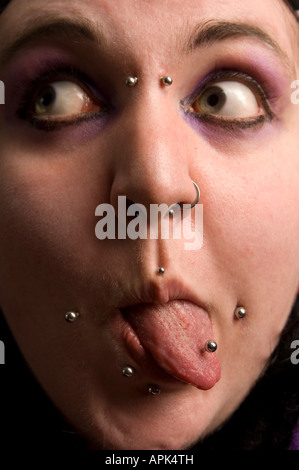 Close up della giovane donna con trafitto viso e lingua fuori la sua linguetta cercando wierd odd bizzarro strani divertenti Foto Stock