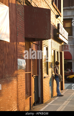 ILLINOIS Chicago giovane donna in attesa appoggiata contro un muro di mattoni di strada di città tardo pomeriggio Foto Stock