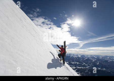 Uomo con lo snowboard sulla sua schiena salendo un bluff in montagna, Austria Foto Stock