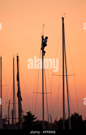 Maschio si stagliano contro il cielo mentre si sale e si lavora su un montante di barche a vela Foto Stock