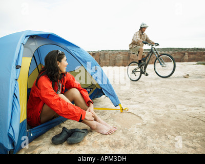 Donna seduta nella tenda, uomo equitazione mountain bike in background Foto Stock