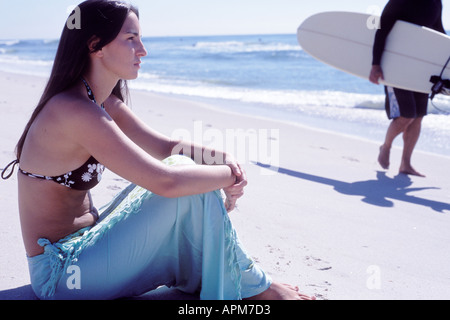 Giovane donna seduta sulla spiaggia con surfer, Long Island USA Foto Stock