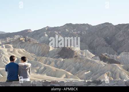 Giovane seduto sul muro di pietra nel deserto (vista posteriore), Death Valley, California, Stati Uniti d'America Foto Stock