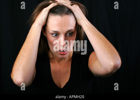 Bruna giovane donna che guarda scioccato storditi sorpreso confuso incredula tenendo le mani sul suo capo con black tshirt Foto Stock