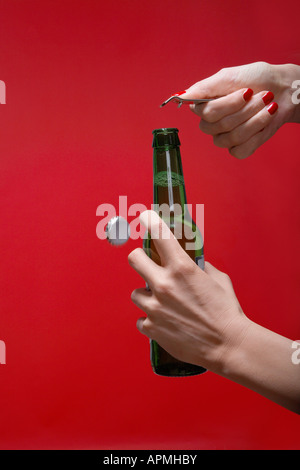 Giovane donna con le mani in mano di aprire una bottiglia di birra (close-up) Foto Stock