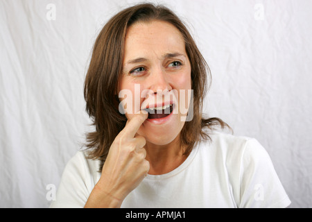 Giovane donna con il dito in bocca che soffrono di malattie croniche mal di denti dolore smorfie in agonia e del disagio Foto Stock