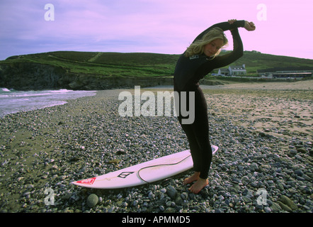 Surfista femmina stiramento sulla spiaggia, Cornwall Foto Stock