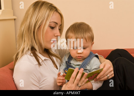 Madre che legge un libro al bambino in grembo di dieci mesi Foto Stock