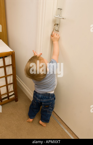 bambino di undici mesi che cerca le chiavi che tenta di sbloccare la porta Foto Stock