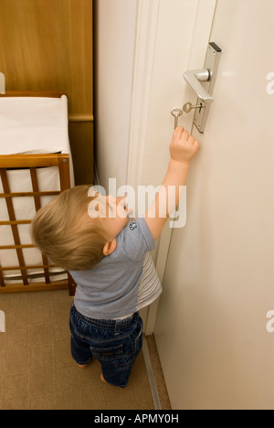 bambino di undici mesi che cerca le chiavi che tenta di aprire la porta, camera non sicura Foto Stock