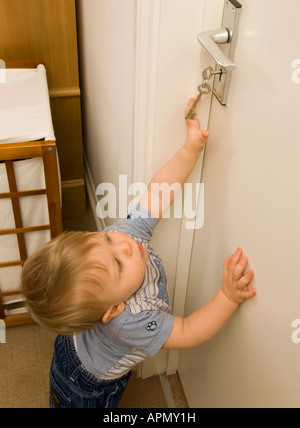 bambino di undici mesi che cerca le chiavi che tenta di sbloccare la porta Foto Stock